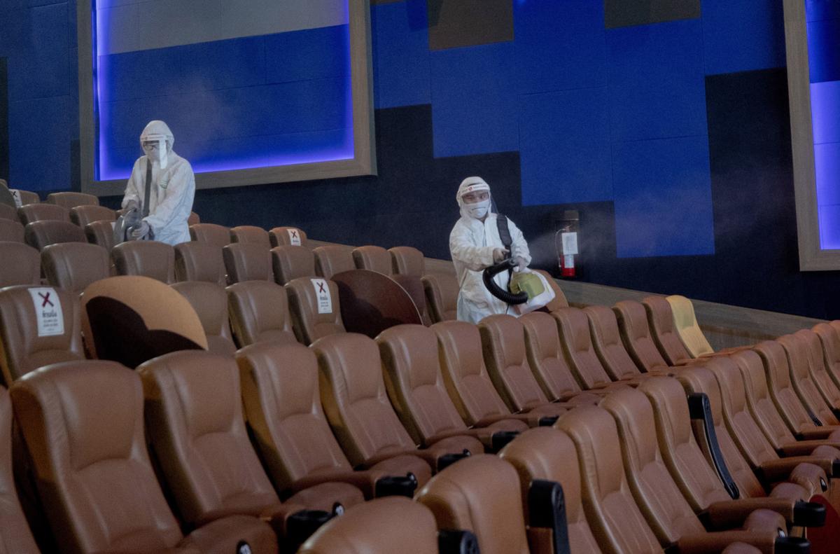 Dua petugas dengan APD sedang menyemprotkan disinfektan di kursi penonton bioskop